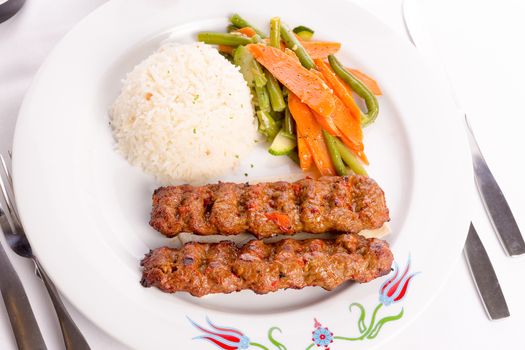 Turkish Adana Kebap with rice pilaf and vegetables served on a Plate