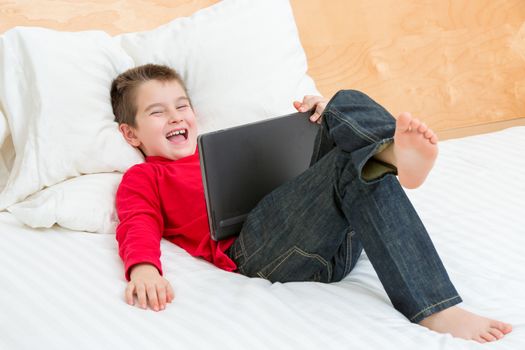 Eight years old boy laughing hard while learning in the bed with his jean and red sweatshirt