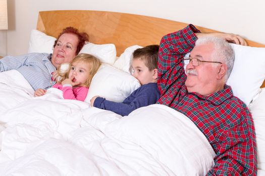 Grandparents watching TV in the bed with their grand kids, they look excited, perhaps its an adventure movie