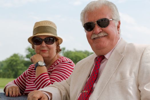 Retired senior couple relaxed and looking at you with their eyeglasses, man wearing suit and tie, woman in her nice striped shirt