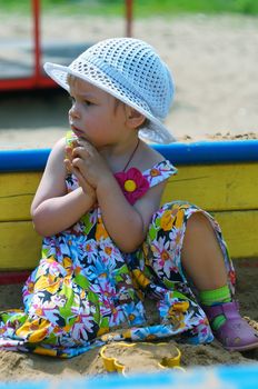 Two-year-old girl sitting in the sandbox and sympathetically looking away                 