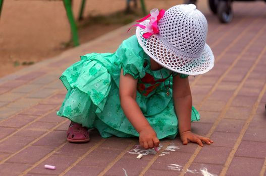 Two-year-old girl draws a chalk on the street            