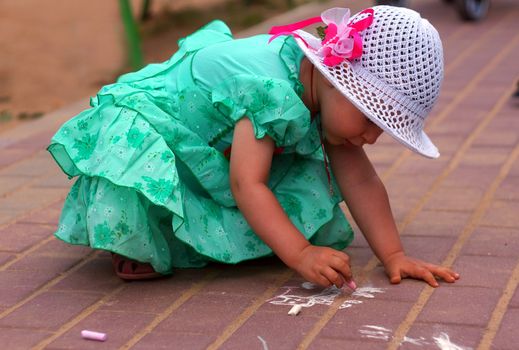 Two-year-old girl draws a chalk on the street