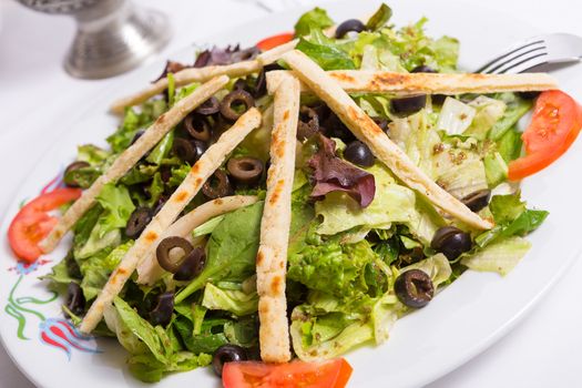 Mediterranean salad with sliced olives, lettuce, spinach tomatoes and olive oil seasoning and arranged with pita slices