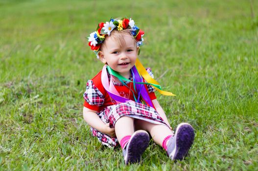 Two-year-old girl sitting on the grass in natsionanom Ukrainian wreaths