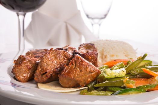 Macro shot of shish kebabs garnished with vegetables and rice pilaf, napkin and vine glass on the background