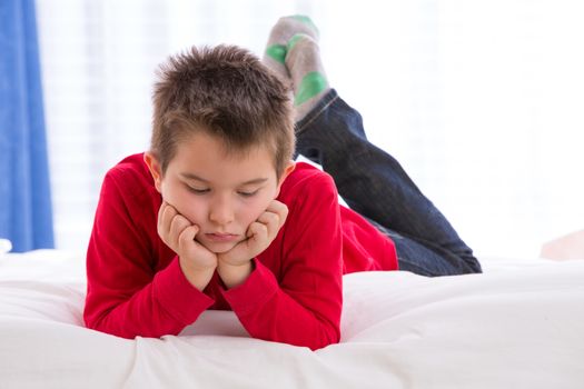 Unhappy kid looking down in the bed with his red sweater and blue jean