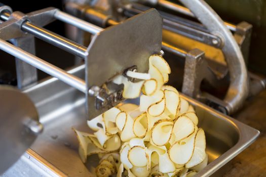 Curly, ribbon potato fries machine in action prepearing potatos for fryer