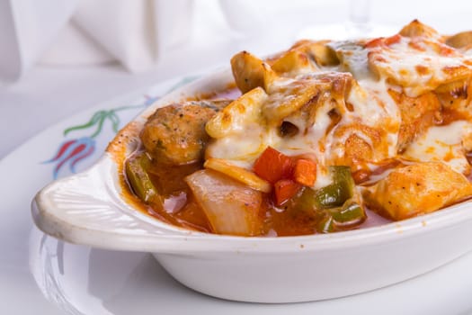 Chicken Saute baked in oven with bell peppers, tomatoes, mushrooms and  chicken meatballs and melted cheese on top of it served in a oval shaped dish