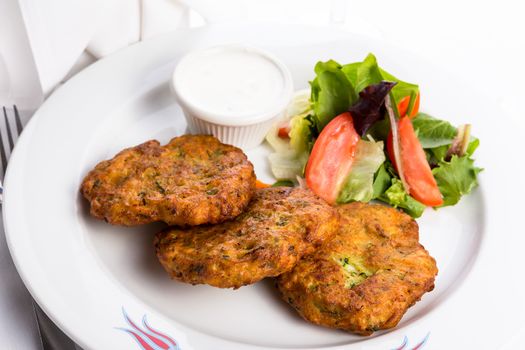 Vegeterian zucchini hash browns served on a white plate and garnished with vegetables