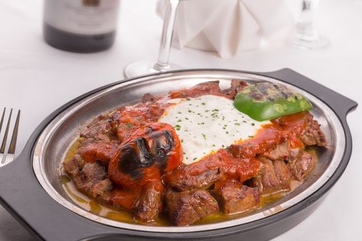 Traditional Turkish Bursa iskender kebap doner served with special red sauce and yogurt in the middle, garnished with grilled tomatoes and peppers