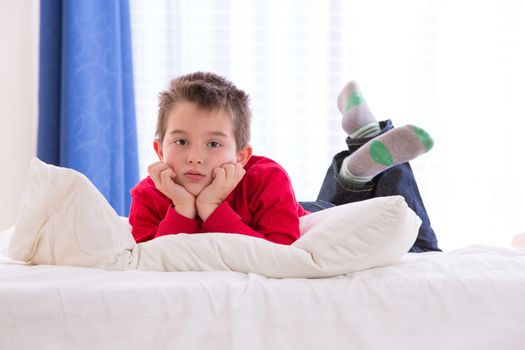 Unhappy kid looking sad in the bed with his red sweater and blue jean