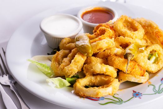 Deep fried breaded calamaries served with white and red sauce and topped with hot pepper pickles