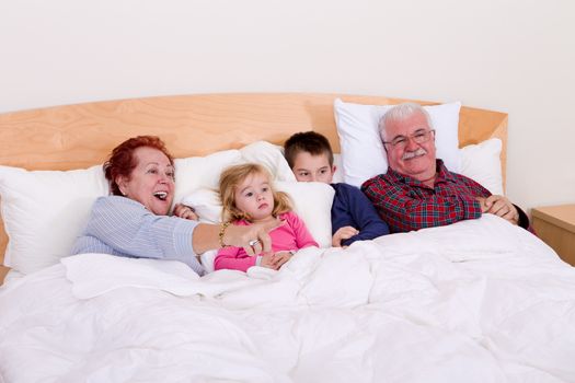 Grandparents watching TV in the bed with their grand kids, they look excited, perhaps its an adventure movie