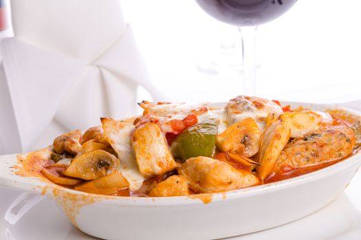 Chicken Saute and melted cheese on top of it served in a oval shaped dish with bell peppers, tomatoes, mushrooms and  chicken meatballs