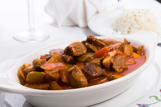 Beef stew with tomatoes, mushrooms and onions served in white oval baking dish