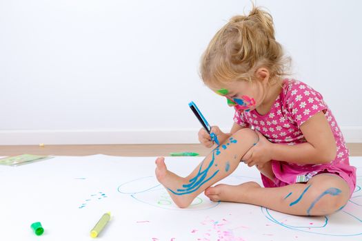 Cute toddler concentrated painting her legs carefully with colorful pens after she painted her face