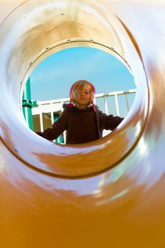 It's a sunny winter day at the other side of the yellow tube slide. Mischievous girl looking down from top of the slide with her coat perhaps getting ready to slide down.