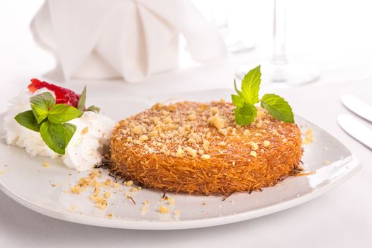 Turkish dessert kunefe with mint leaves, slices strawberry on a full fat cream and pinch of walnuts served after a nice meal