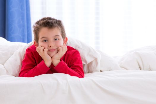 Close up portrait of a eight years old boy laying on the bed on looking at  you in his bedroom at home. He looks calm and relaxed.
