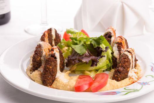 Fried half cut falafel patties of finely ground garbanzo beans spiced with parsley, cilantro and onion, laid on hummus and garnished with tomato slices and lettuce