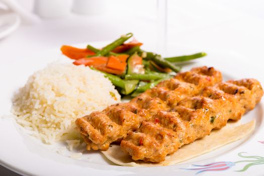 Chicken Adana kebap served with rice pilaf and green vegetables and some carrots