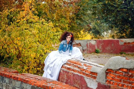 Beautiful bride in wedding dress and denim jacket in autumn park
