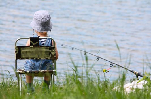 Little boy with fishng rod sitting near the lake