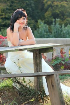 Girl in the wedding dress sitting on the bench neat the table