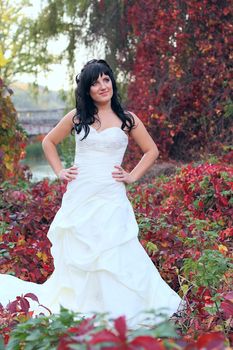 Girl in a weeding dress in a park among green and red leaves