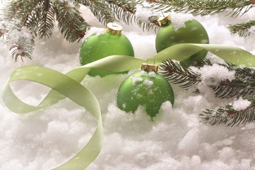 Green holiday balls and ribbon in snow