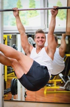 Smiling attractive young man hanging from gym equipment, looking at camera