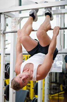 Young man in gym working out, exercising abs by hanging upside-down