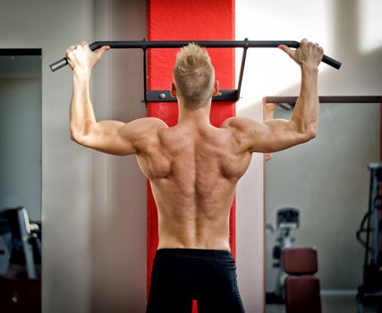 Blond, attractive young man hanging from gym equipment, seen from the back