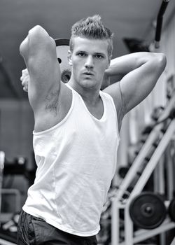 Handsome young man in gym holding and lifting  weight over his head, looking at camera