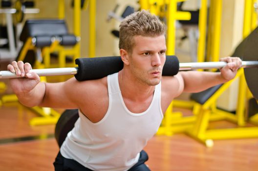 Handsome young man doing squats in gym with barbell