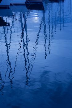 Blue water reflection of sailboats boats poles in waves tranquil water