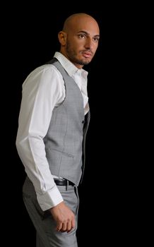 Bald, handsome young man with elegant shirt and vest looking to a side, isolated on black