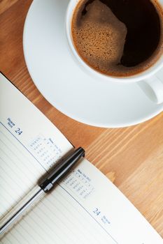 Notebook with pen and cup of coffee on a table. Top view