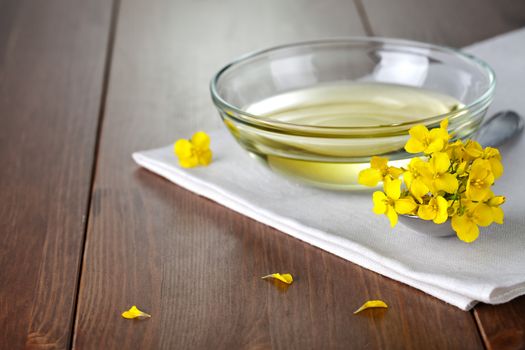 Rapeseed oil in bowl with flower of rapeseed. Food composition on wooden background