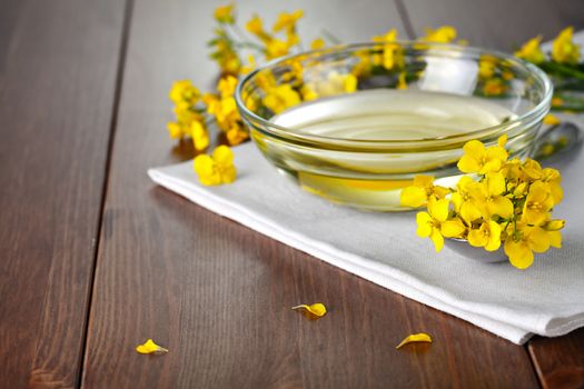 Rapeseed oil with flower of rapeseed. Food composition on wooden table