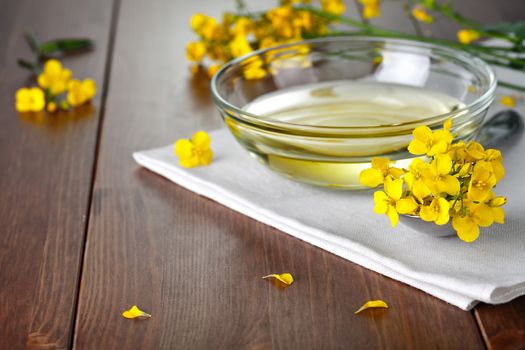 Rapeseed oil and flowers on wood background. Food composition