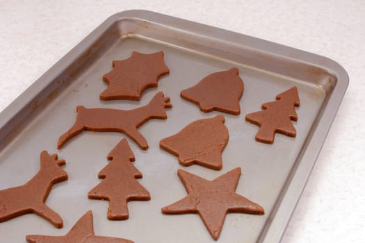 Cookie sheet with uncooked gingerbread biscuits in festive shapes