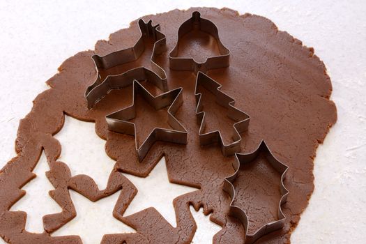 Cookie cutters and cut out shapes on gingerbread dough - star, reindeer, Christmas tree, holly leaf and bell