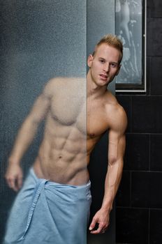 Handsome young man shirtless behind shower glass, with towel around waist