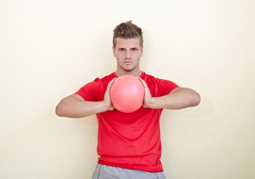 Young man holding exercise ball in his hands on neutral background, looking at camera