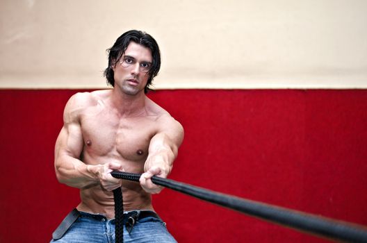 Handsome shirtless muscular man wearing jeans pulling rope indoors