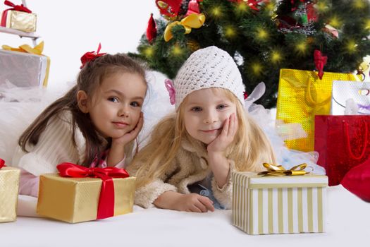 Two cute girls lying under Christmas tree with gifts