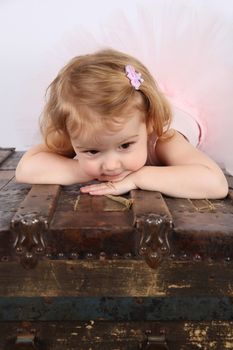 Little ballet girl wearing a pink tutu on an antique trunk