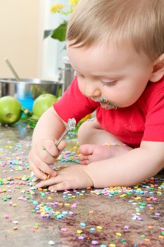 Cute baby boy eating cake decorations on counter top